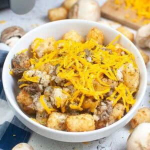 White bowl filled with hamburger potato casserole topped with shredded cheddar cheese.