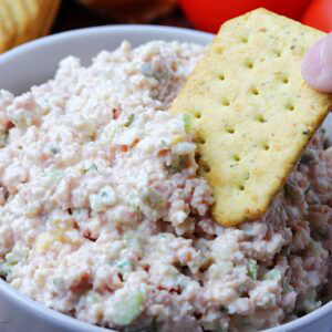 Closeup view of a cracker being dipped into a bowl of old fashioned ham salad.