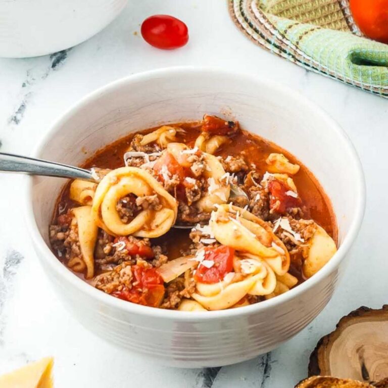 White bowl filled with rustic tortellini soup garnished with shredded parmesan.