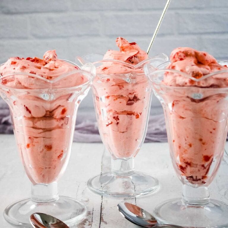 Three decorative sundae glasses filled with strawberry cool whip salad with 2 spoons.