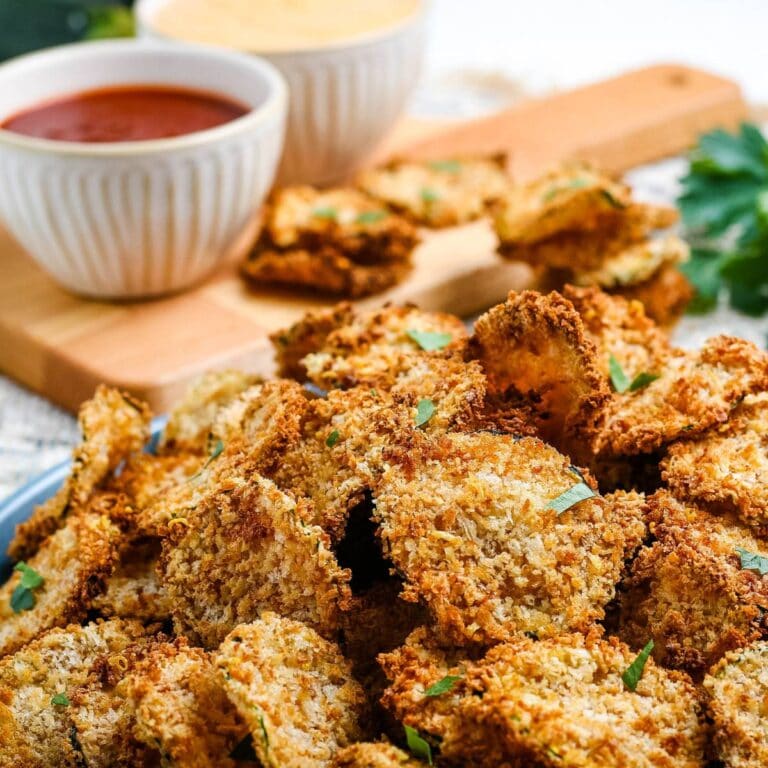 Closeup view of breaded air fryer zucchini chips with bowls of dipping sauce in the background.