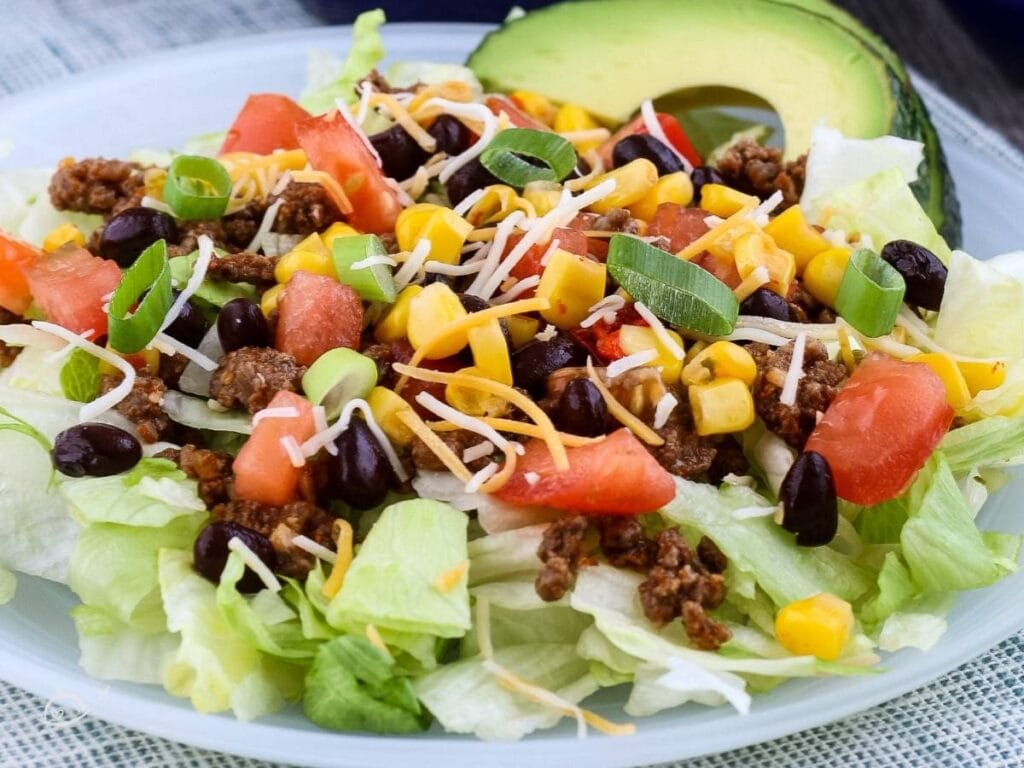 Homemade taco salad garnished with avocado slices on a white plate.