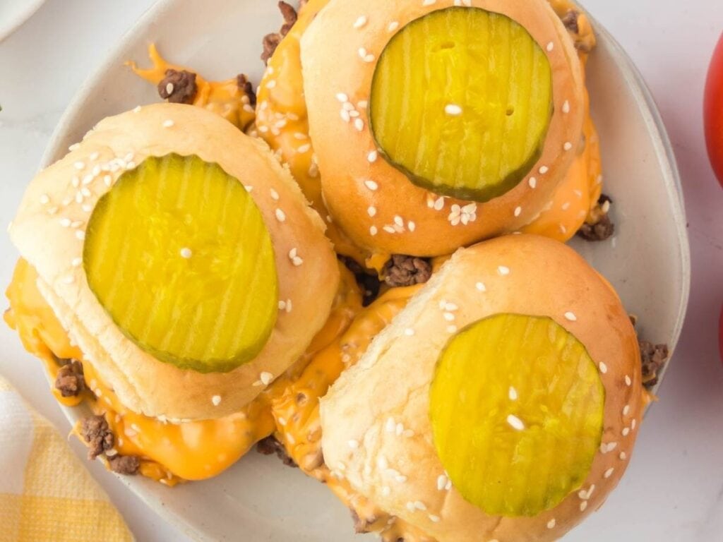 Three loose meat cheeseburger sliders topped with pickle chips.