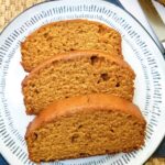 Three slices of spiced pumpkin bread with vanilla pudding on a decorative white plate.