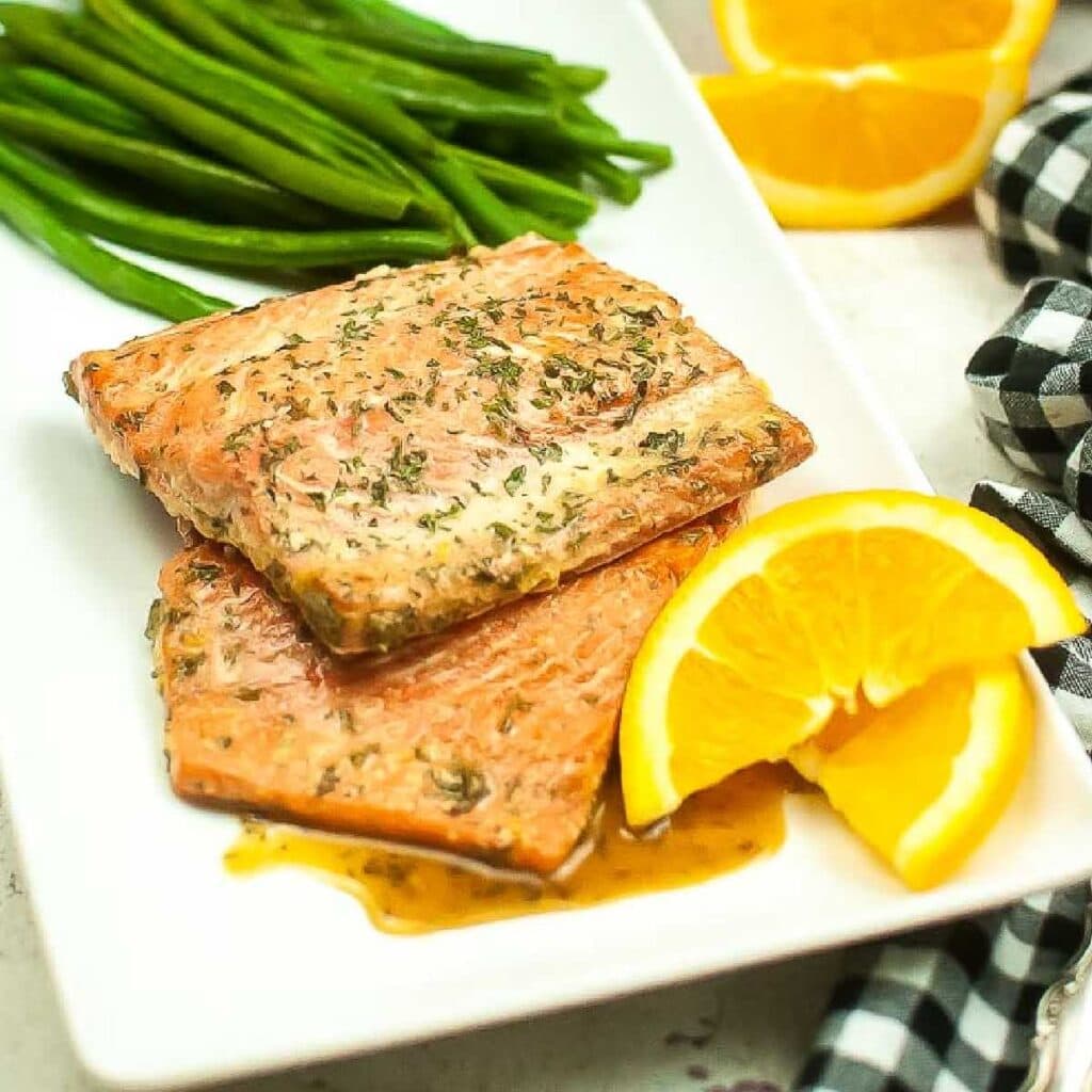 Front view of a white plate filled with air fryer honey orange glazed salmon filets with orange slices and green beans.