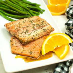 Front view of a white plate filled with air fryer honey orange glazed salmon filets with orange slices and green beans.