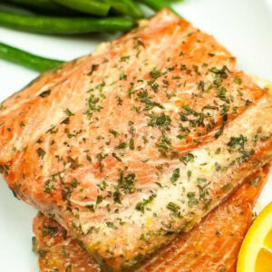 Closeup view of 2 pieces of glazed salmon on a white plate with orange slices and green beans.