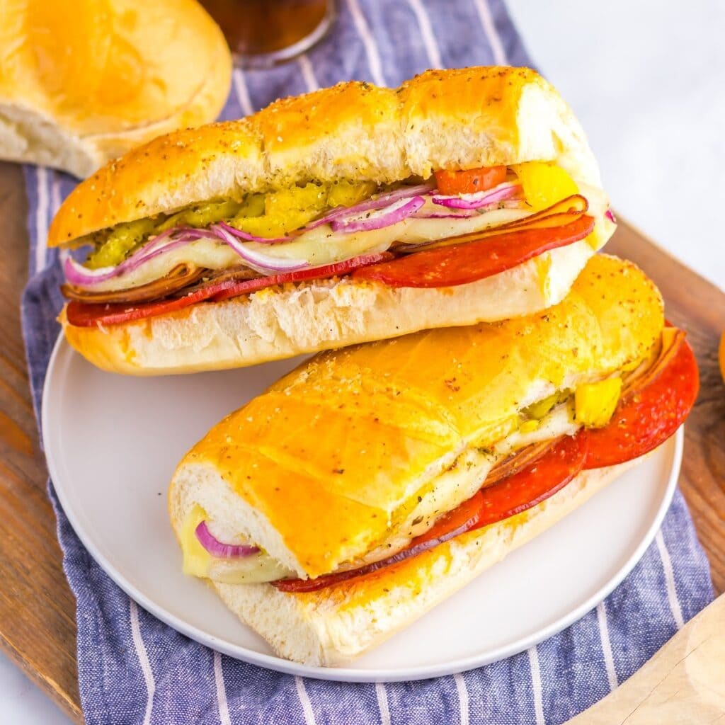 Baked Italian subs on a white plate with a striped dish towel underneath.