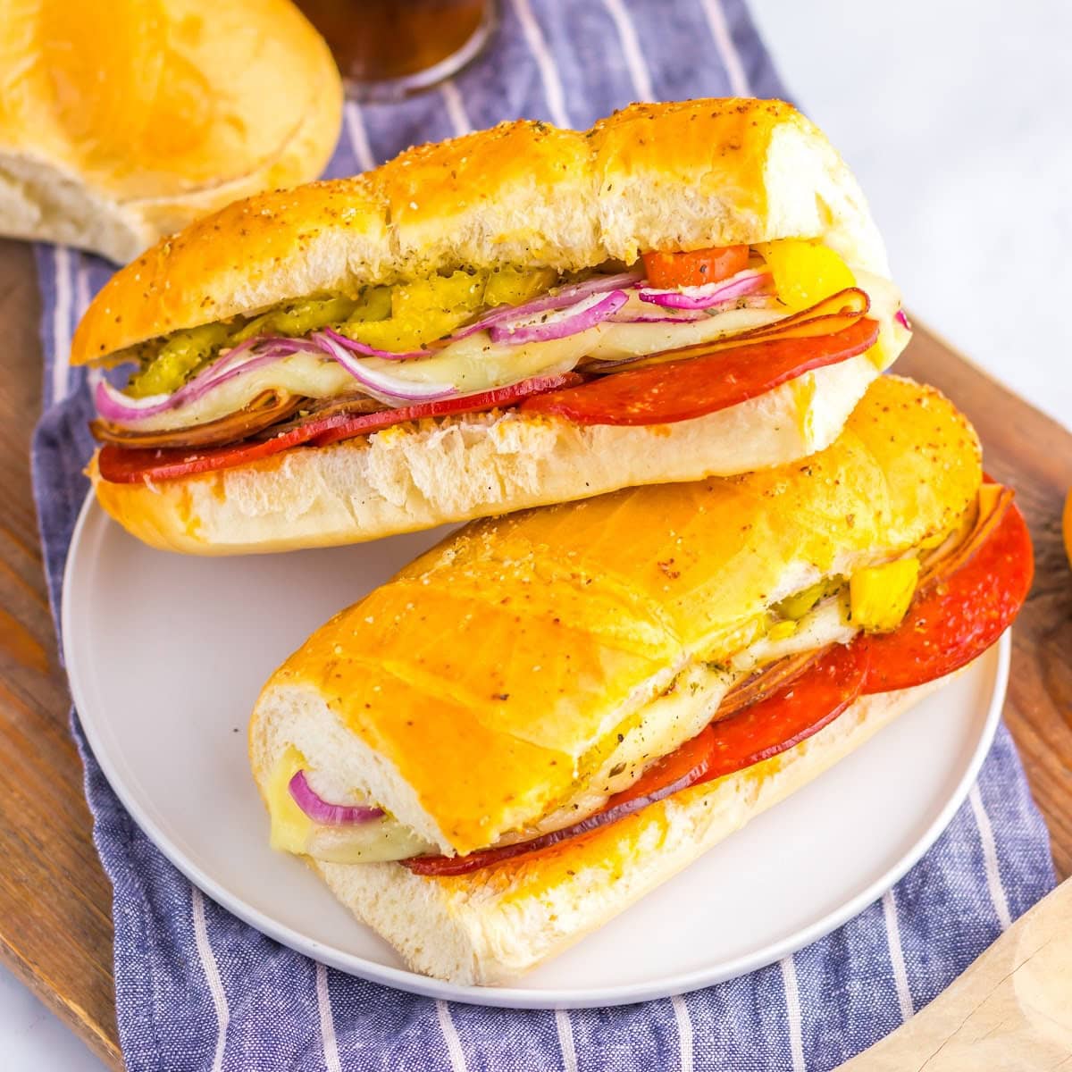 Baked Italian subs on a white plate with a striped dish towel underneath.