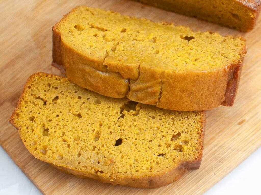 Two slices of vanilla pudding spiced pumpkin bread on a wooden cutting board.