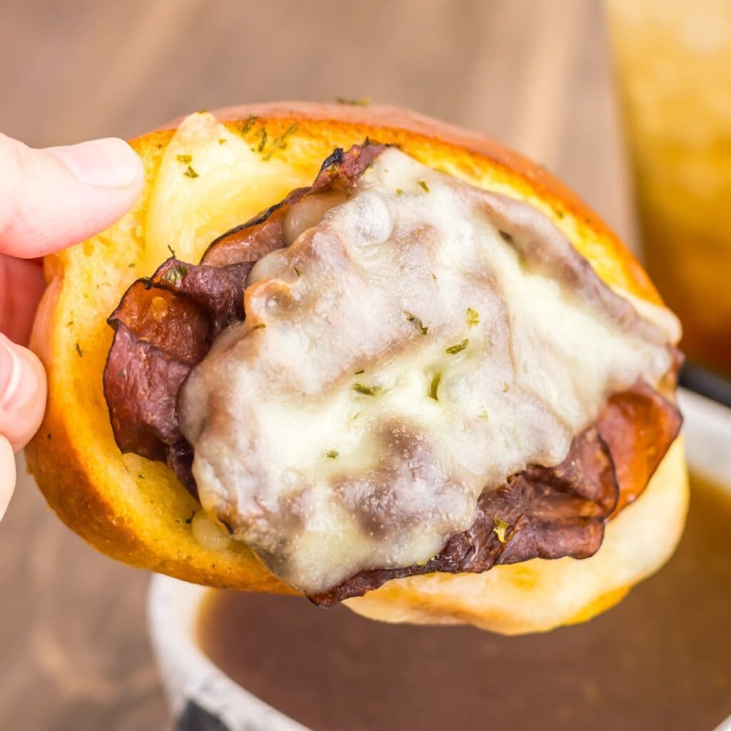 Close-up of a garlic bread French dip sandwich topped with melted provolone cheese and roast beef, ready to dip in au jus.