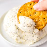 Close-up of a cracker being dipped into homemade Boursin cheese spread.