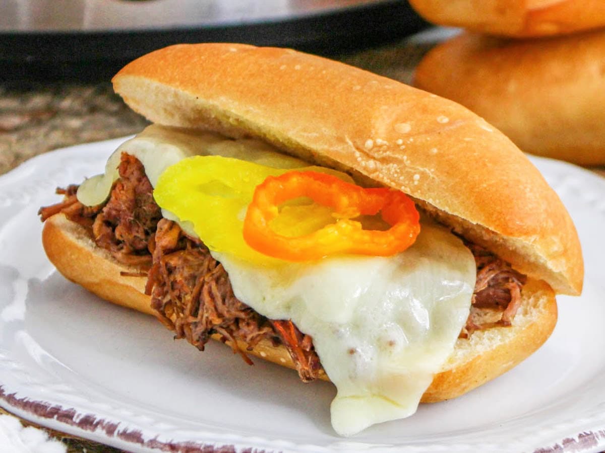 Crockpot Italian beef hoagies melted provolone and garnished with pepperoncini peppers on a toasted roll.