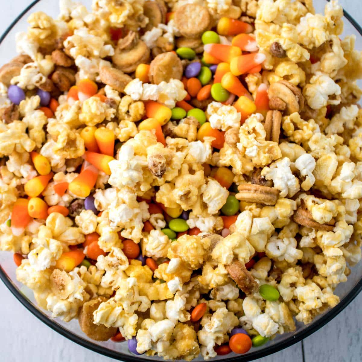 Clear bowl filled with sweet and salty fall snack mix with popcorn, candy corn, peanuts and candy coated chocolates.