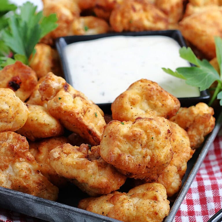 Closeup view of air fryer popcorn chicken pieces with a bowl of ranch dipping sauces.