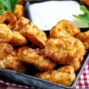 Closeup view of pieces of breaded popcorn chicken with a bowl of ranch dipping sauce.