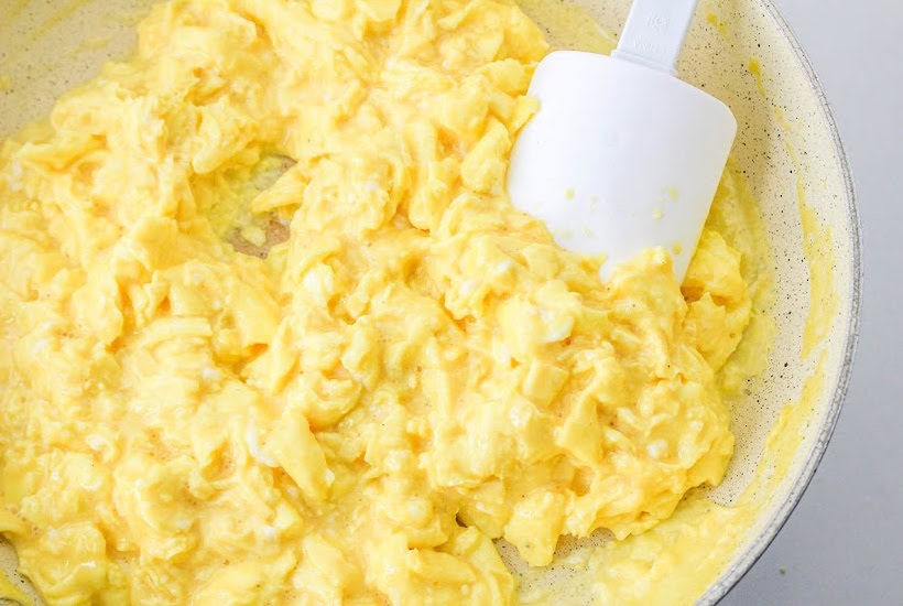 Cooking scrambled eggs in a skillet with a white spatula.