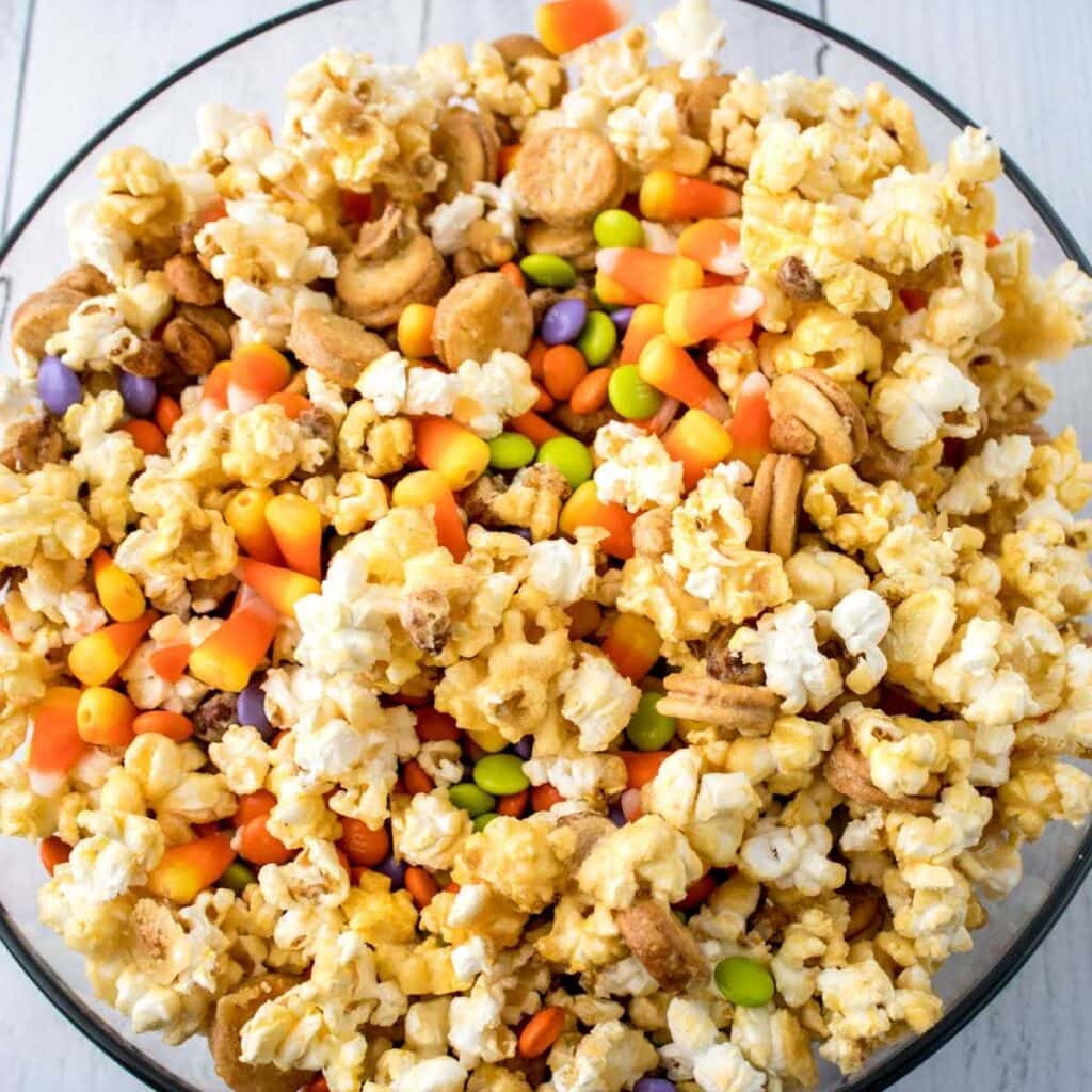 Overhead view of a clear bowl filled with sweet and salty fall snack mix with popcorn.