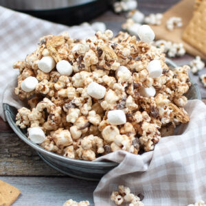Closeup view of homemade smores popcorn in a metal bowl with a tan checked napkin.