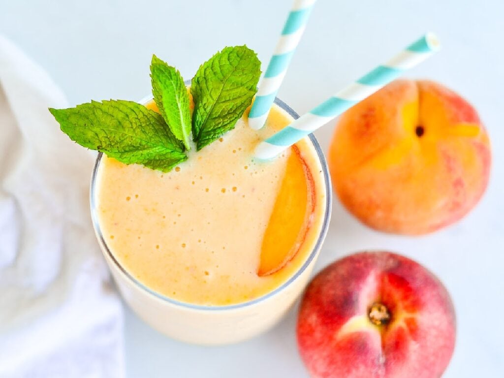 Top view of a homemade fresh peach smoothie next to whole  fresh peaches.