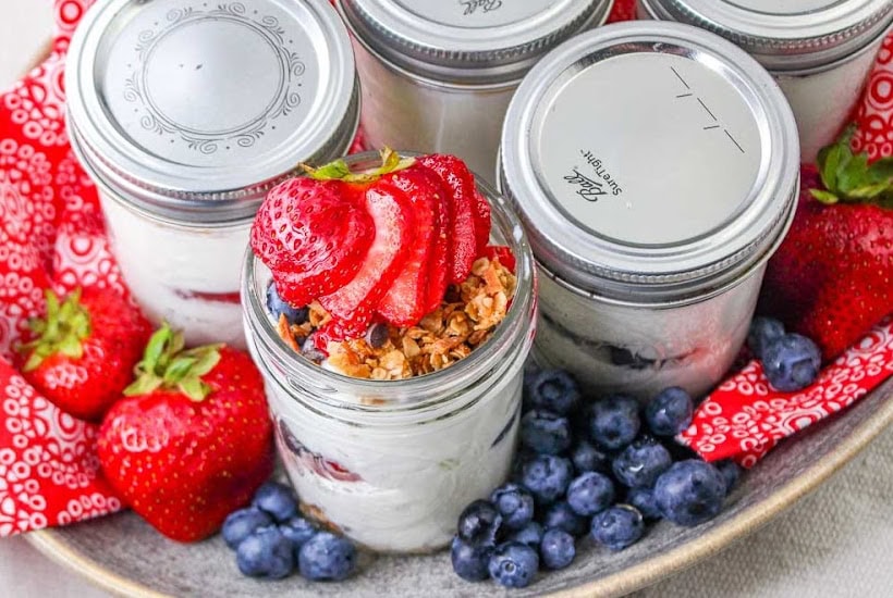 Make ahead yogurt parfaits topped with granola and strawberries in a serving tray next to blueberries.
