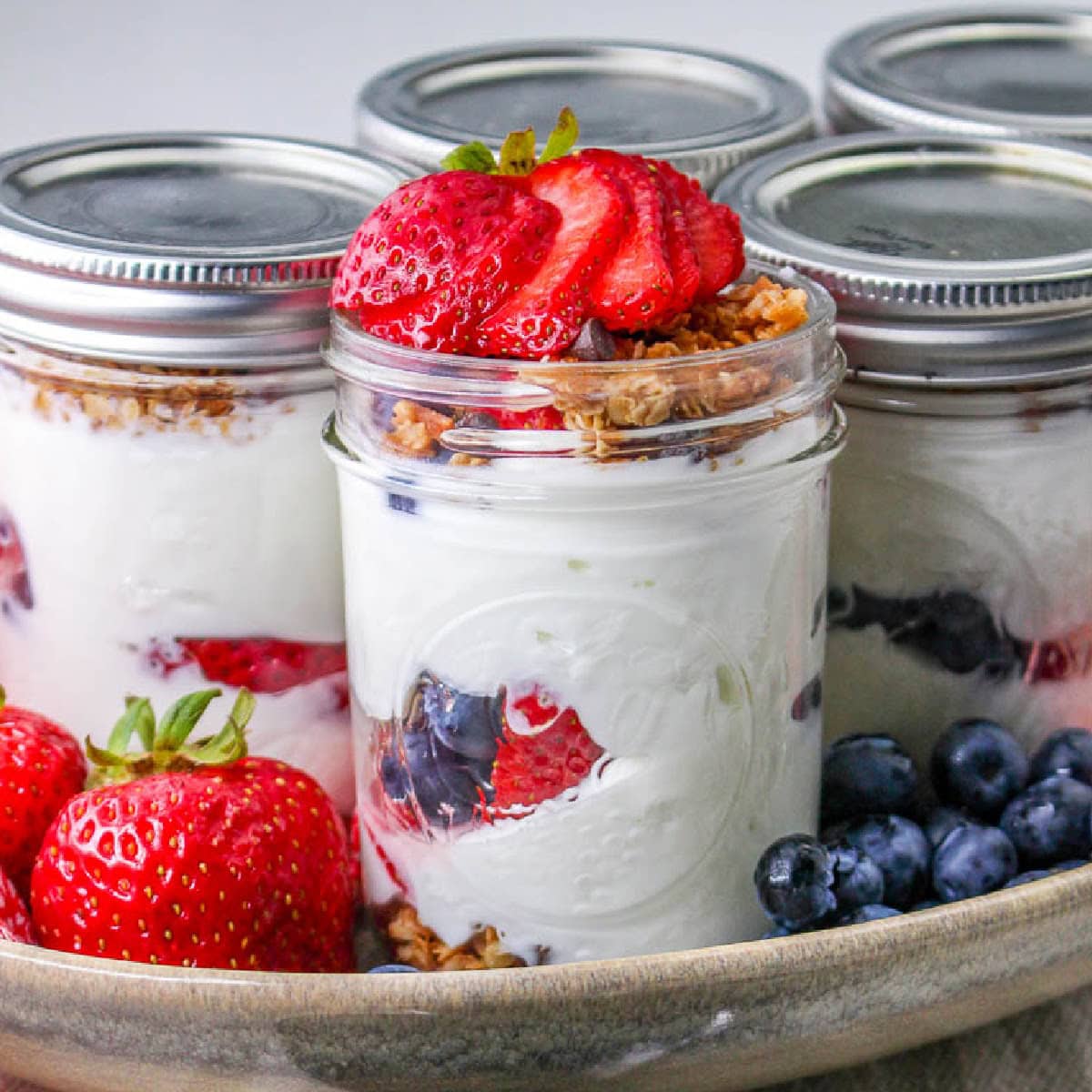 Make ahead greek yogurt parfaits in mason jars, one with the lid off topped with berries and granola.