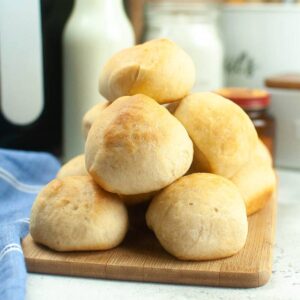 Soft air fryer dinner rolls with yeast stacked on a wood cutting board.