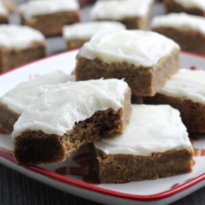 Gingerbread blondies with cream cheese frosting stacked on a holiday plate.