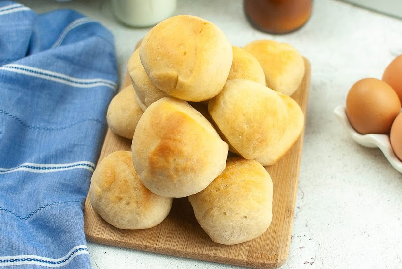Homemade air fried yeast rolls on a cutting board next to a blue towel.