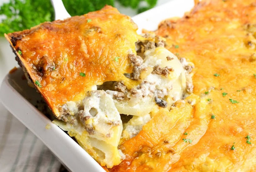 Scooping out a slice of cheesy hamburger and potato casserole from the dish.