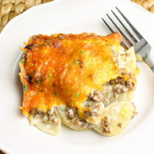 A scoop of cheesy hamburger potato casserole on a white plate with a fork.