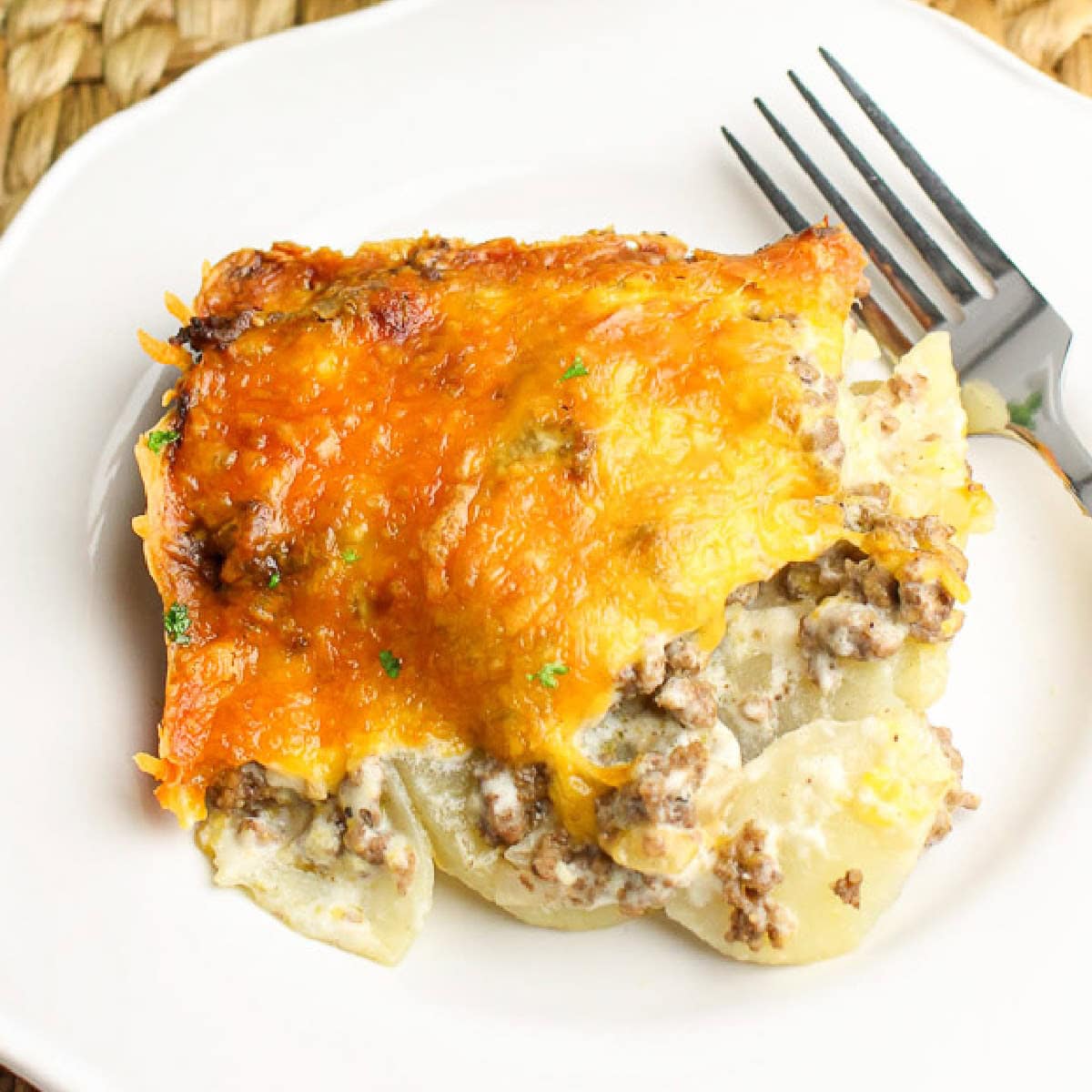 A scoop of cheesy hamburger potato casserole on a white plate with a fork.