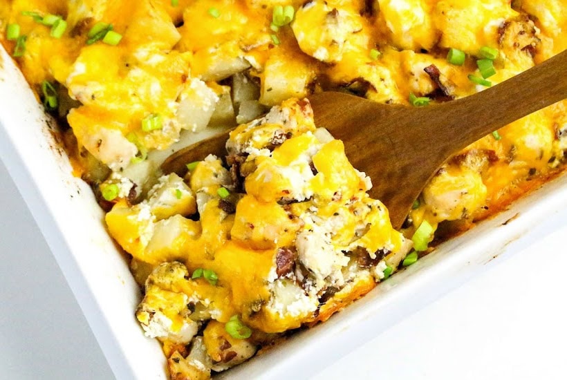 Scooping out the chicken bacon potato ranch casserole from the casserole dish with a wooden spoon.