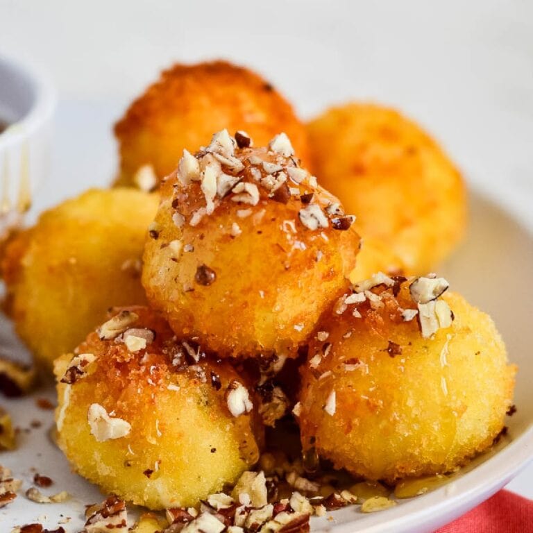 Closeup view of fried goat cheese balls garnished with chopped pecans and honey and stacked on a plate.