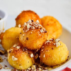 Fried goat cheese balls with breading and garnished with chopped pecans and stacked on a white plate.