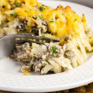 Close up of hamburger hash brown casserole on a white plate with a fork cutting in.