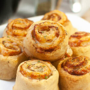 Top view of air fryer ham and cheese pinwheels stacked on a white plate.