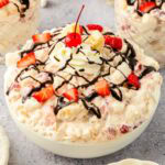 Banana split fluff salad topped with sliced strawberries, chocolate drizzle, whipped cream, and a cherrie.