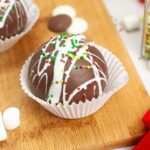 Closeup overhead view of Christmas Hot Cocoa Bombs in a paper cupcake holder on a wooden cutting board.