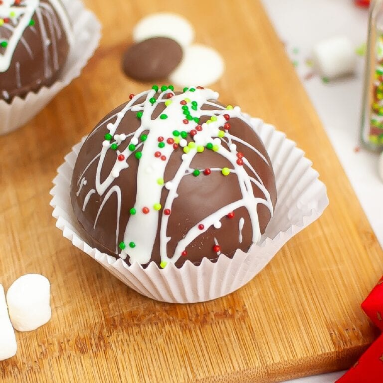 Closeup overhead view of Christmas Hot Cocoa Bombs in a paper cupcake holder on a wooden cutting board.