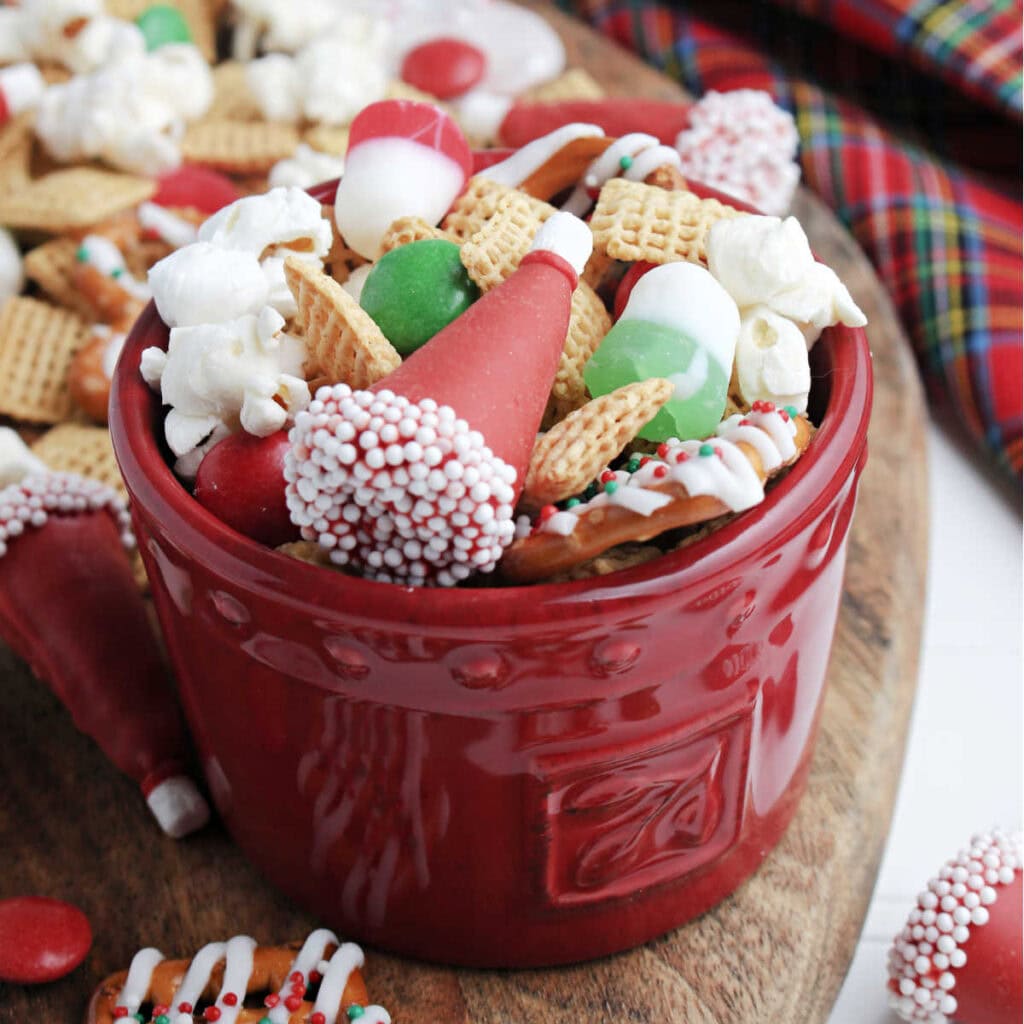 Closeup view of a red bowl filled with Christmas Snack mix with Santa hats and pretzels.