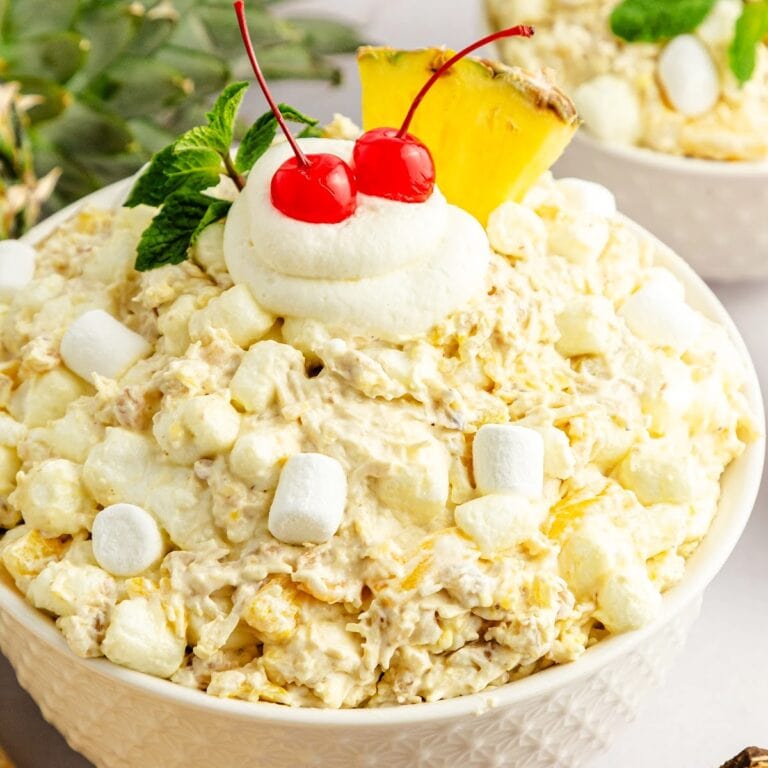 Pina colada fluff salad topped with extra marshmallows, Cool Whip, cherries, and a pineapple wedge.