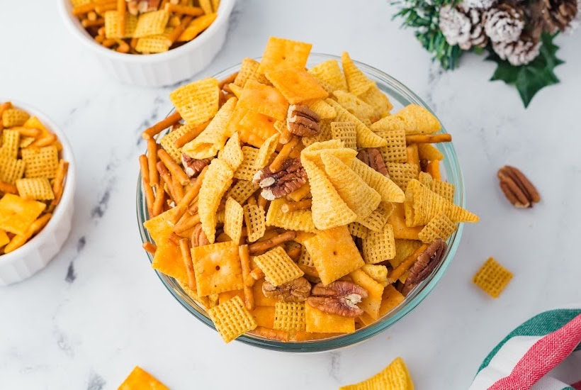 Overhead view of a bowls of reindeer snack mix with bugles, cheese crackers, pretzels, Chex cereal and pecans.