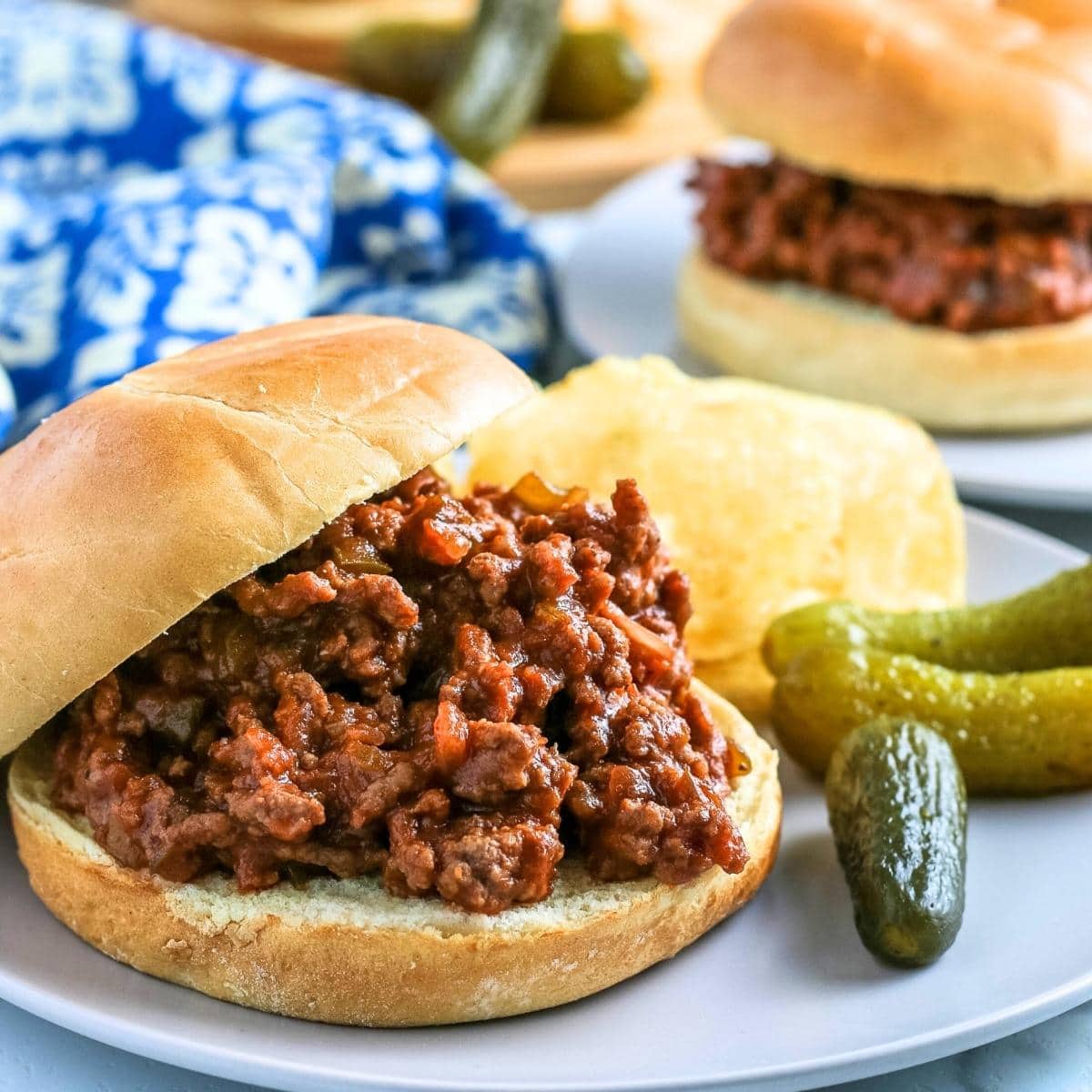 Crock pot sloppy joes on burger buns with potato chips and pickles.