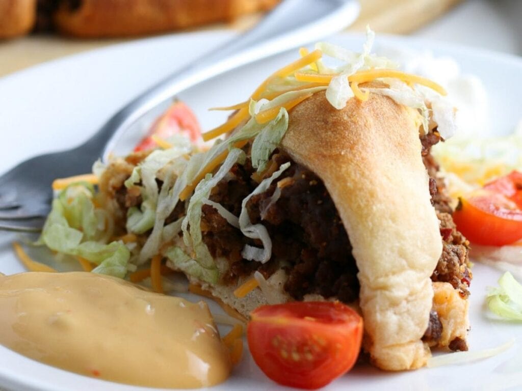 Closeup view of a slice of taco ring garnished with lettuce, cheese and dipping sauce.