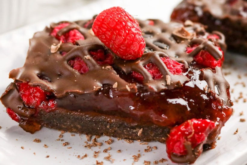 Raspberry chocolate squares on a white serving dish topped with fresh berries.