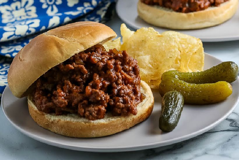 Closeup view of homemade sloppy joes on buns with chips and pickles.