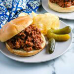 An old fashioned sloppy Joe on a bun with potato chips and pickles.