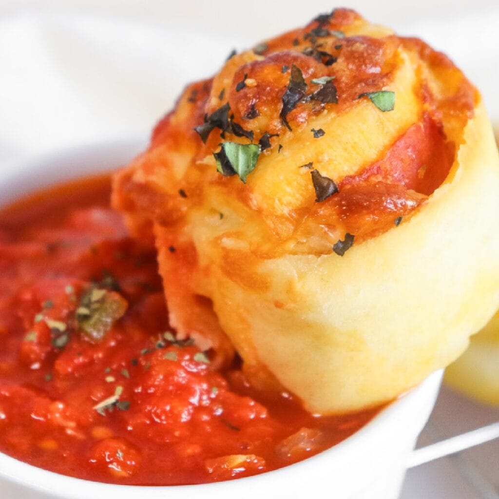 Homemade pepperoni pinwheel being dipped into marinara sauce.