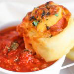 Homemade pepperoni pinwheel being dipped into marinara sauce.